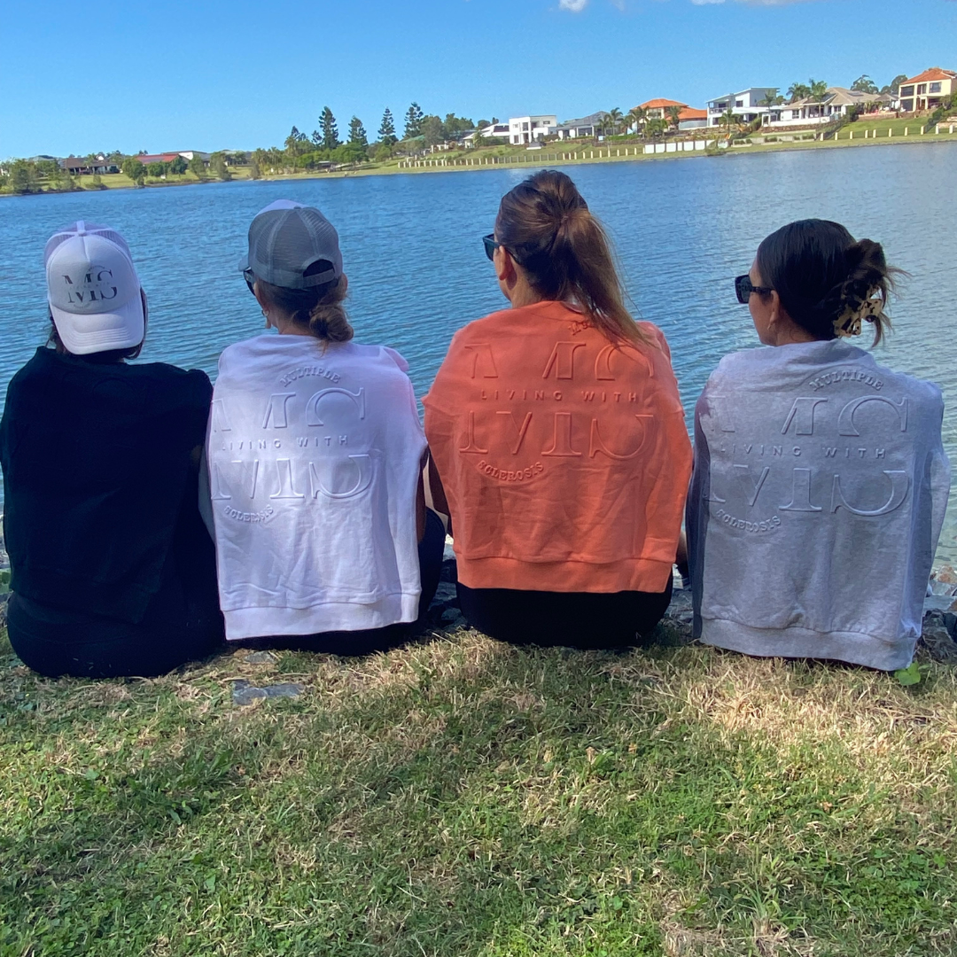 4 figures sitting down with Living with embossed jumpers round their shoulders in Black, White, Orange and Grey