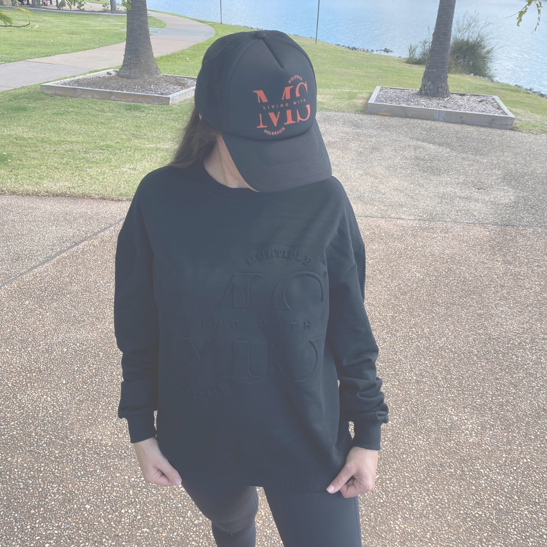 Figure wearing Black embossed sweater and Black trucker cap with Orange Logo