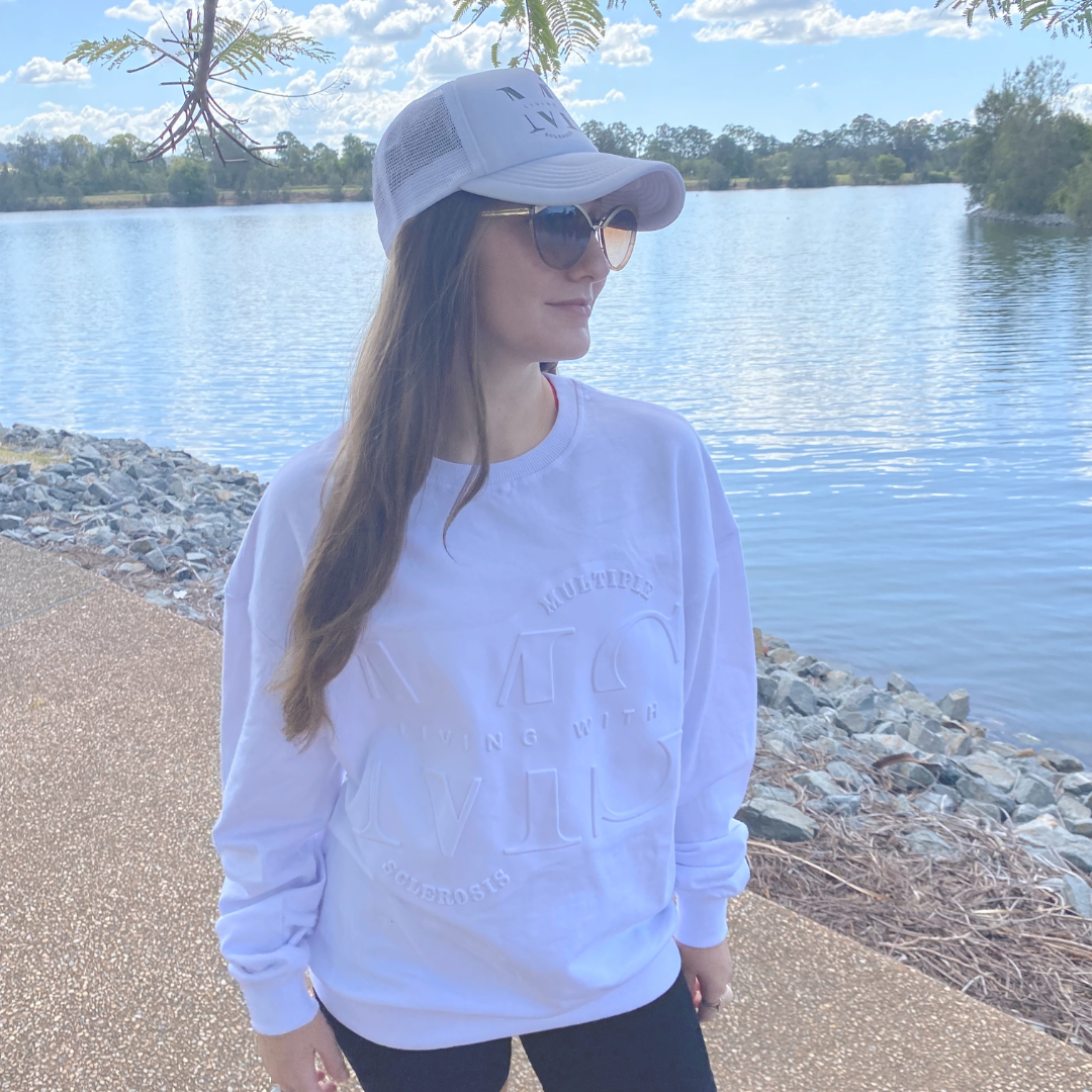 Figure wearing white embossed sweater with white trucker cap with grey logo